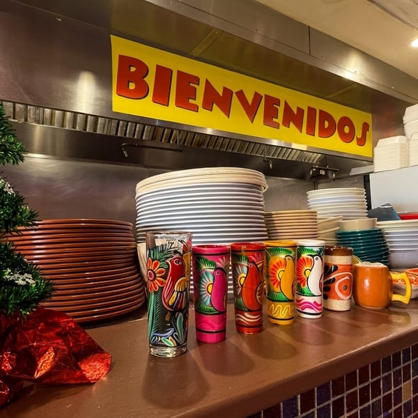 A small Christmas tree and colorful Mexican-themed glasses on a restaurant counter with a "BIENVENIDOS" sign.
