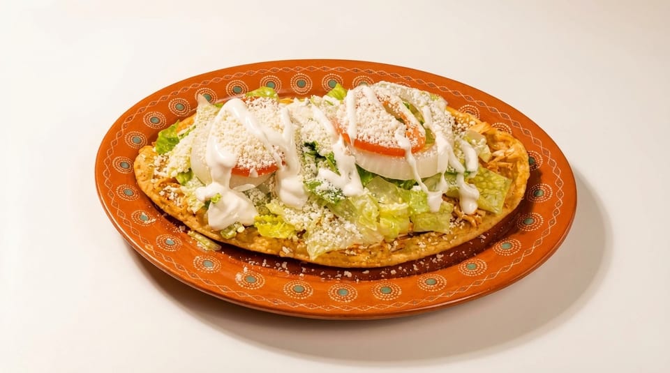 A large tostada with shredded chicken, lettuce, tomato, onion, sour cream, and crumbled cheese.