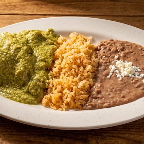 A plate of green chile chicken, Spanish rice, and refried beans topped with cotija cheese.